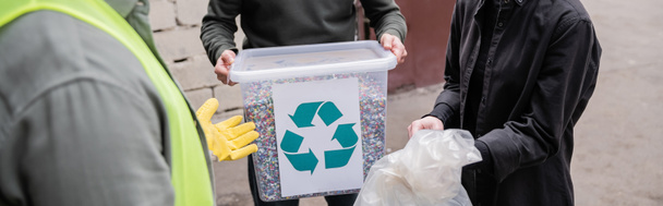 Widok pracownika w kamizelce ochronnej i rękawicy stojącego w pobliżu wolontariuszy ze śmieciami w zewnętrznym składowisku odpadów, koncepcja sortowania i recyklingu śmieci, baner  - Zdjęcie, obraz