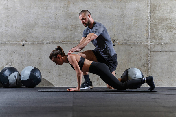 A muscular man assisting a fit woman in a modern gym as they engage in various body exercises and muscle stretches, showcasing their dedication to fitness and benefiting from teamwork and support. - Photo, Image