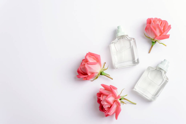 Due bottiglie di profumo e fiori di rosa su sfondo bianco. Bellezza, concetto di moda. Vista dall'alto, disposizione piatta, spazio di copia. - Foto, immagini