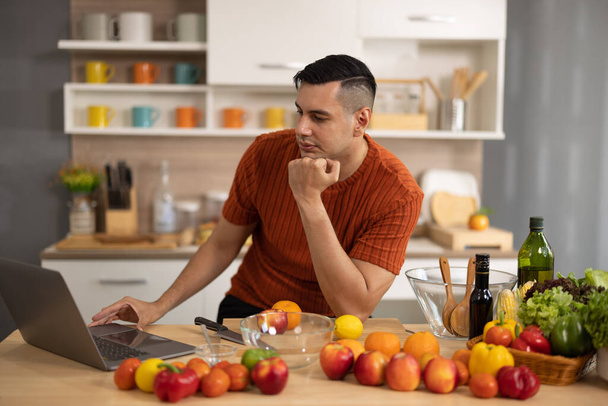 A homely and healthy male prepares nutritious diet, including variety of fruits. Following cooking show on laptop Mastery of peeling, chopping, and slicing fruits to prepare them in artistic style. - 写真・画像