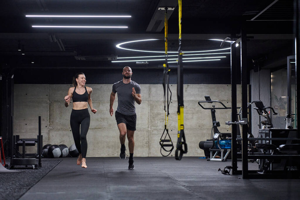 Een fit koppel in een moderne fitnessruimte, bezig met hardloopoefeningen en presenteren van hun atletische dapperheid met een dynamische start - Foto, afbeelding