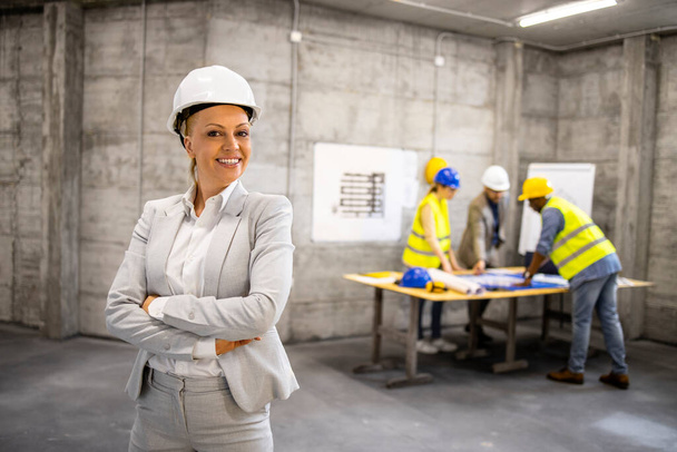 Portrait of successful female architect in business suit and hard hat standing at construction site. - Foto, Imagem