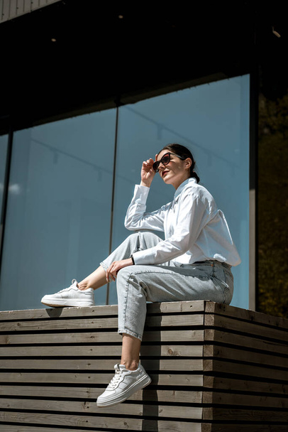 Pretty woman in a white shirt and glasses posing against the backdrop of a modern mountain hotel.Businessman woman concept - Фото, изображение