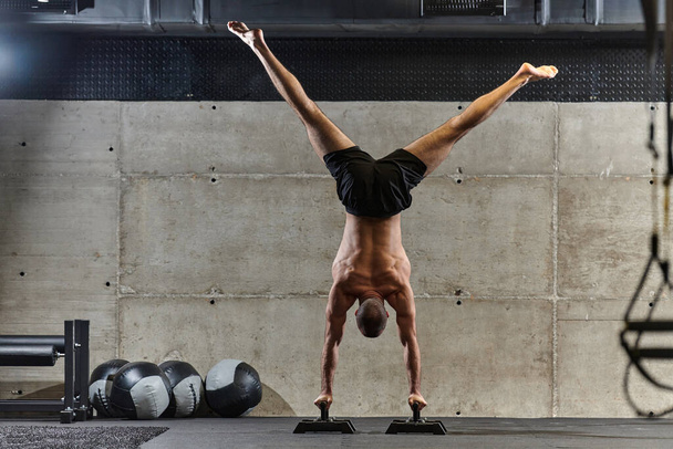 A muscular man in a handstand position, showcasing his exceptional balance and body control while performing a variety of exercises to enhance his overall body stability and strength in a modern gym. - Zdjęcie, obraz