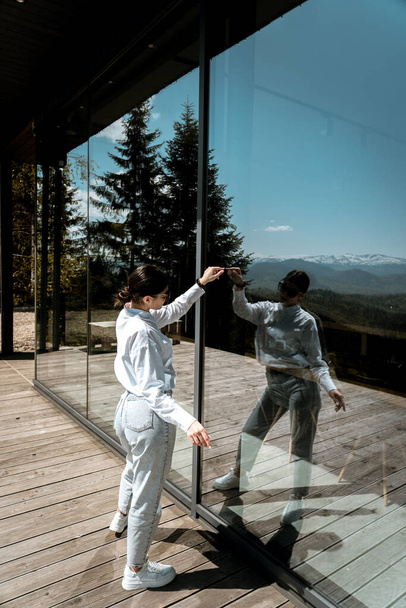 Hübsche Frau in weißem Hemd und Brille posiert vor der Kulisse eines modernen Berghotels. - Foto, Bild