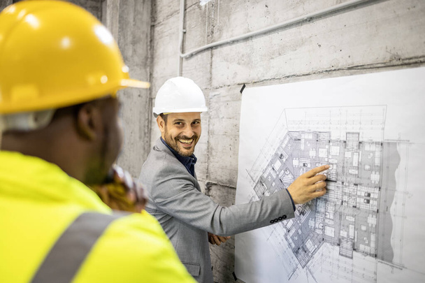 Obrero de la construcción e ingeniero civil teniendo reunión en el sitio y mirando el plano del edificio. - Foto, imagen