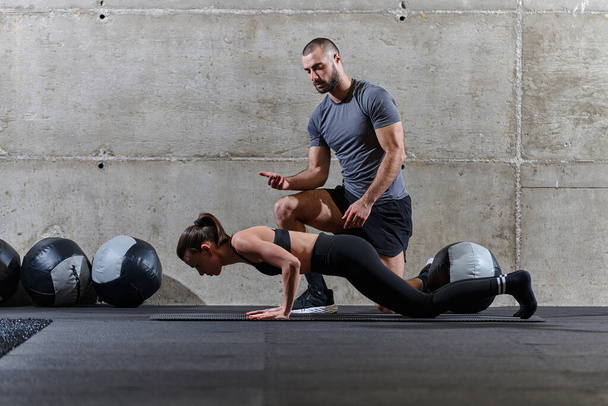 A muscular man assisting a fit woman in a modern gym as they engage in various body exercises and muscle stretches, showcasing their dedication to fitness and benefiting from teamwork and support. - Foto, imagen