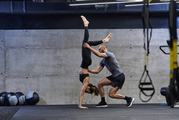 A muscular man assisting a fit woman in a modern gym as they engage in various body exercises and muscle stretches, showcasing their dedication to fitness and benefiting from teamwork and support. - Foto, afbeelding