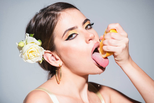 Closeup portrait of beautiful girl with oranges and colored makeup. Sexy woman with stylish makeup on beautiful face squeezing juice from fresh orange, lick orange juice - Photo, image