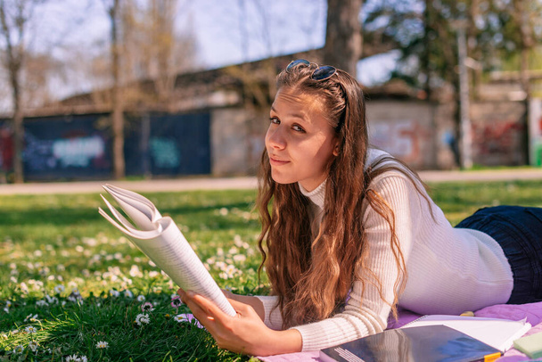 Hübsches brünettes Mädchen liest Buch und schaut in die Kamera - Foto, Bild