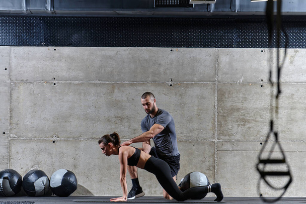 A muscular man assisting a fit woman in a modern gym as they engage in various body exercises and muscle stretches, showcasing their dedication to fitness and benefiting from teamwork and support. - Foto, Imagem