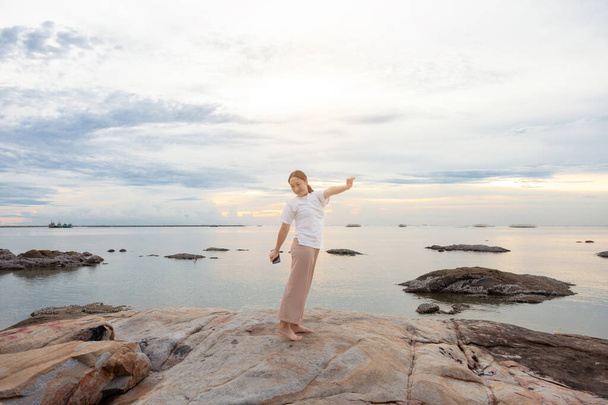 Азійська жінка зі смартфонами розслабилася і підняла руку на пляжі. жінка розслабляється і дихає свіжим повітрям. Щаслива мандрівниця азіатка звільняє негативні емоції від лінивого ранку, мирного вихідного.. - Фото, зображення