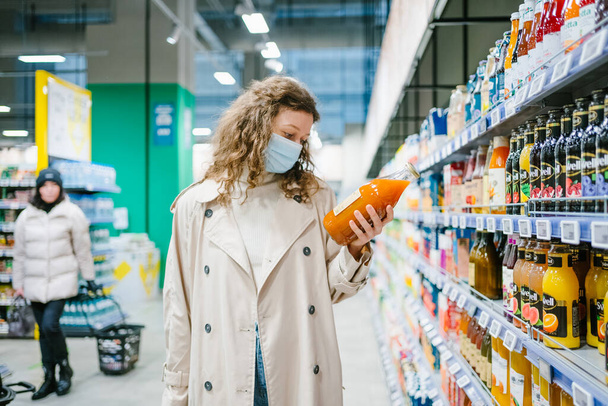 Genç bayan müşteri bir süpermarkette kabak havucu suyu etiketinin üzerindeki kompozisyonu dikkatle okuyor. Uygun beslenme kavramı ve katkı maddeleri olmadan kaliteli ürünlerin seçimi ve - Fotoğraf, Görsel