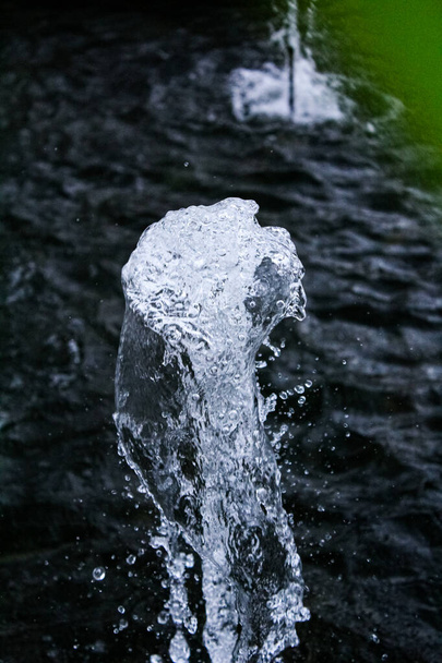 Water fountain springs, water spout of fountain pool in a park. the texture of waterdrops. Transparent frozen visible drops of water in the air. The movement and fragment of a splashing water stream - Foto, imagen