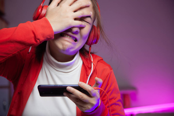 Mujeres asiáticas gamer con auriculares jugando juego móvil en el teléfono inteligente en línea. streamers profesionales de streaming de juegos en el juego de juego social que lamenta haber perdido el juego. Estilo de luces de neón cibernético - Foto, imagen