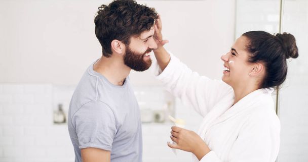 Couple, face skincare cream and bathroom with smile, helping hand and morning together in home. Woman, man and skin wellness for help, care or laughing with product for lifestyle, beauty or health. - Foto, Bild