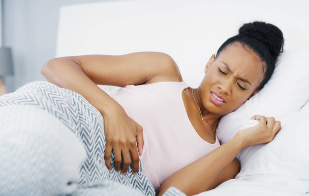 Stomach, pain and problem with woman in bed for menstruation, medical and pms. Endometriosis, healthcare and period with person suffering in bedroom at home for uncomfortable, bloated and sad. - Photo, Image
