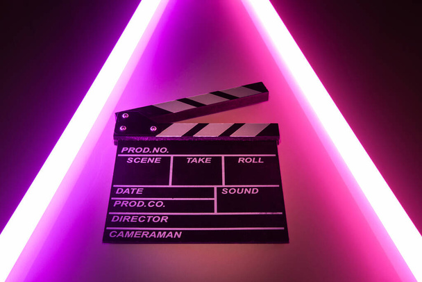 Klaszczotka film łupek na Świecące neonowe oświetlenie tła. reżyser filmowy kręcący film. Element projektu klapki filmowej. klaśnięcie filmowca, aby film wideo - Zdjęcie, obraz
