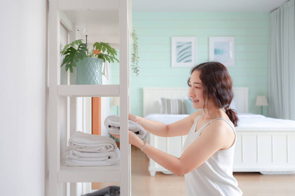 Azjatka sprzątająca nowoczesny dom. Szczęśliwa kobieta wykonująca domowe obowiązki. Azji gospodyni składanie ubrania w szafie. - Zdjęcie, obraz