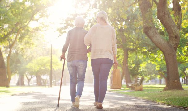 Walking, park and and woman with elderly mother for bonding, assistance and help outdoors. Nature, family and female person with disability with cane and adult daughter for wellness, relax or support. - Photo, Image