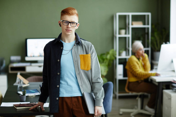 Талия портрет рыжеволосый молодой человек в ярком стиле и улыбаясь на камеру в офисе, копировать пространство - Фото, изображение