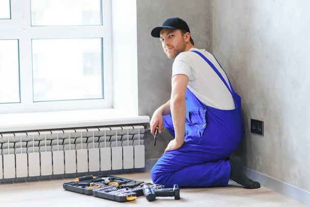 young man plumber checking radiator while installing heating system in apartment. - Valokuva, kuva