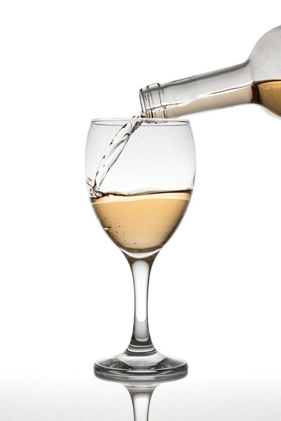 A bottle filling a white wine glass over a reflective surface over a white background - Fotografie, Obrázek