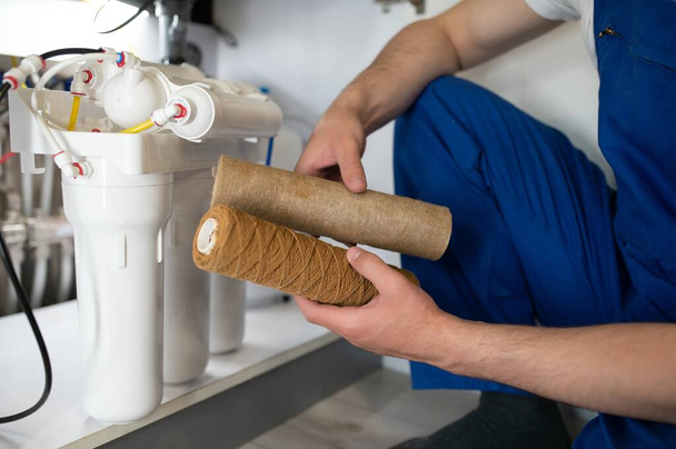 Plumber installs or change water filter. Replacement aqua filter. Repairman installing water filter cartridges in a kitchen. Installation of reverse osmosis water purification system - Foto, Imagem