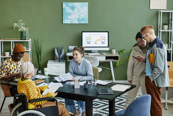 Retrato de un equipo creativo diverso trabajando en la oficina con una mujer joven usando silla de ruedas en una reunión de negocios - Foto, imagen