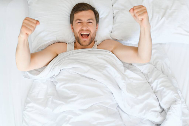 Cheerful Man Waking Up Lying In Cozy Bed At Home On Weekend Morning. Healthy Sleep Concept. - Fotografie, Obrázek