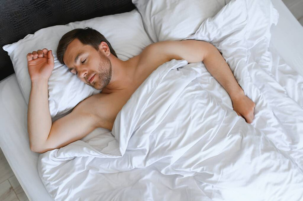 Handsome man sleeping under soft blanket in bed at home. - Photo, Image