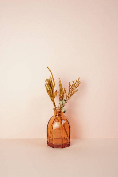 Bruine glazen vaas van droge bloem op roze tafel. roze muur achtergrond. kopieerruimte - Foto, afbeelding