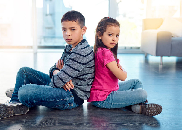 Portrait, children and sitting with arms crossed after fight, anger and backs together on floor in house. Angry, brother and sister in home living room, fighting or argument, conflict or problem - 写真・画像