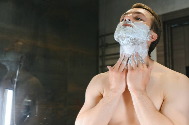 Shaving cream. Morning hygiene procedures. Grooming treatment. Handsome cheerful shirtless man showing applying foam on skin. - Photo, image