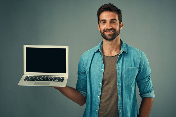 Szczęśliwy człowiek, laptop i ekran makietowy do reklamy lub marketingu na szarym tle studio. Portret mężczyzny z uśmiechem na ekranie komputera lub pozorem miejsca na reklamę. - Zdjęcie, obraz