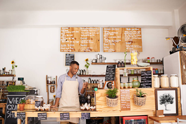 Μαύρος, υπάλληλος καφετέριας και τηλέφωνο ενός επιχειρηματία με ευτυχία από τις μικρές επιχειρήσεις. Cafe, κινητό και barista αναζητούν μουσική εφαρμογή για το τραγούδι με χαμόγελο στο φούρνο και το εστιατόριο αίσθημα ευτυχίας. - Φωτογραφία, εικόνα