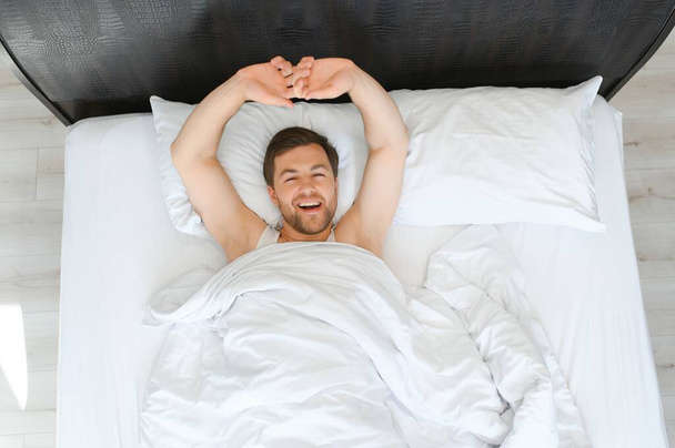 Happy young bearded man is relaxing on the bed at home. - Foto, Bild