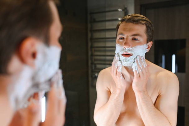Shaving cream. Morning hygiene procedures. Grooming treatment. Handsome cheerful shirtless man showing applying foam on skin. - Foto, imagen