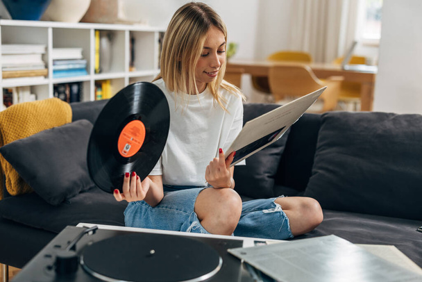 A blond woman is reading titles of songs on the cover of a record. - Zdjęcie, obraz