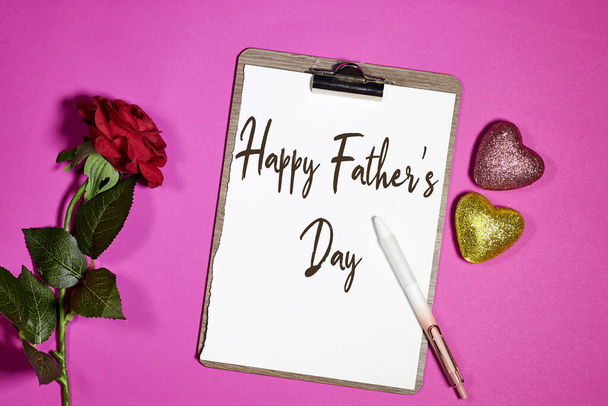 gelukkige vaderdag op klembord met rode roos bloem en glitter harten op roze achtergrond - Foto, afbeelding