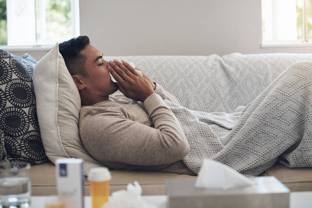 Het griepseizoen is hier. een jonge man snuit zijn neus terwijl hij zich ziek voelt thuis - Foto, afbeelding