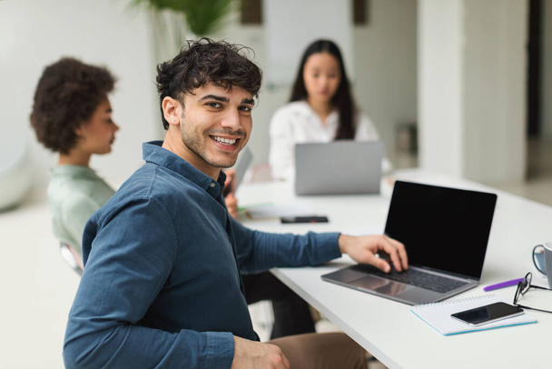 Successful Career. Cheerful Middle Eastern Businessman Using Laptop Sitting At Corporate Meeting With Diverse Coworkers Women In Modern Office, Smiling To Camera. Selective Focus - Foto, imagen