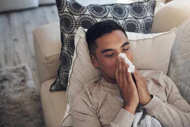 Looks like Im going to go through many tissues today. a young man blowing his nose while feeling sick at home - Фото, изображение