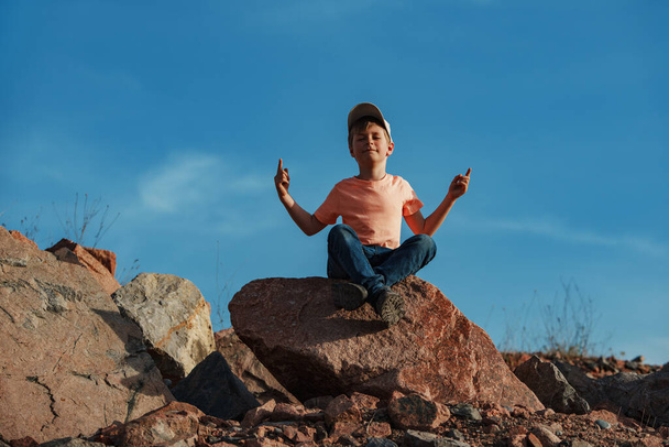Boy sitting in meditation pose on rock in the mountains - Foto, immagini
