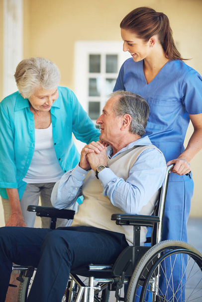 Yaşlı bir eş, bakıcı ya da hastane kliniğinde tekerlekli sandalyedeki yaşlı bir adam mutlu bir hastaya yardım ediyor. Gülümse, olgun kadın ya da sağlık görevlisi engelli bir ihtiyarla konuşuyor.. - Fotoğraf, Görsel