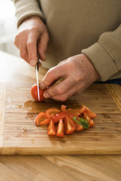 cooking, food and home concept - close up of male hand cutting tomato on cutting board at home - Zdjęcie, obraz