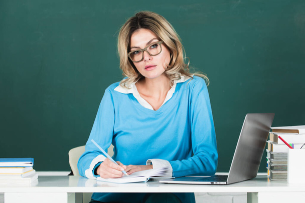 Female teacher. Sensual student woman in eyeglasses near blackboard. Sexy girl sit on table on chalkboard. Attractive female teacher in college - Foto, imagen