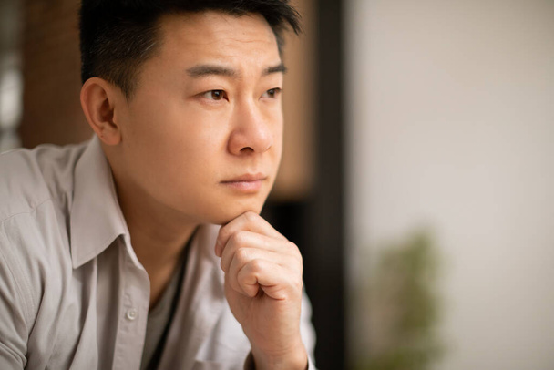 Closeup of unhappy asian middle aged man sitting alone at home, leaning on his arm, have heavy thoughts, experiencing midlife crisis, going through divorce, copy space - Foto, Imagem
