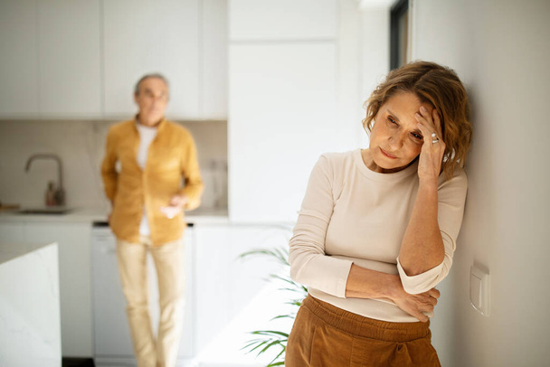 Upset elderly caucasian couple standing in kitchen after argue, senior man and woman having domestic conflicts, suffering relationship crisis, selective focus on aged crying lady - Фото, изображение