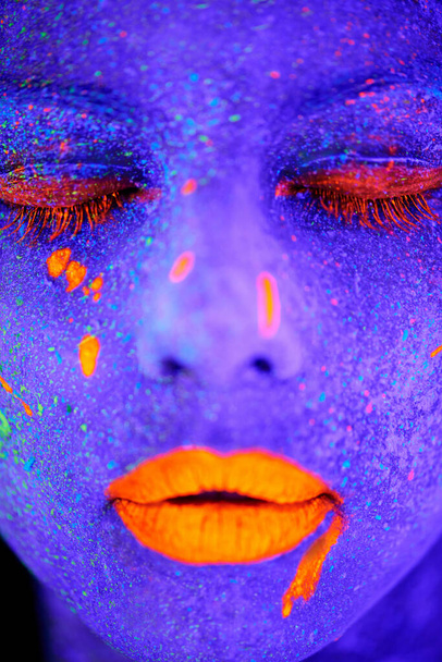 Neon paint, beauty and woman face closeup with dark background and creative cosmetics. Glow, rave makeup and psychedelic cosmetic of a female model with unique and creativity with art in studio. - Foto, Imagem